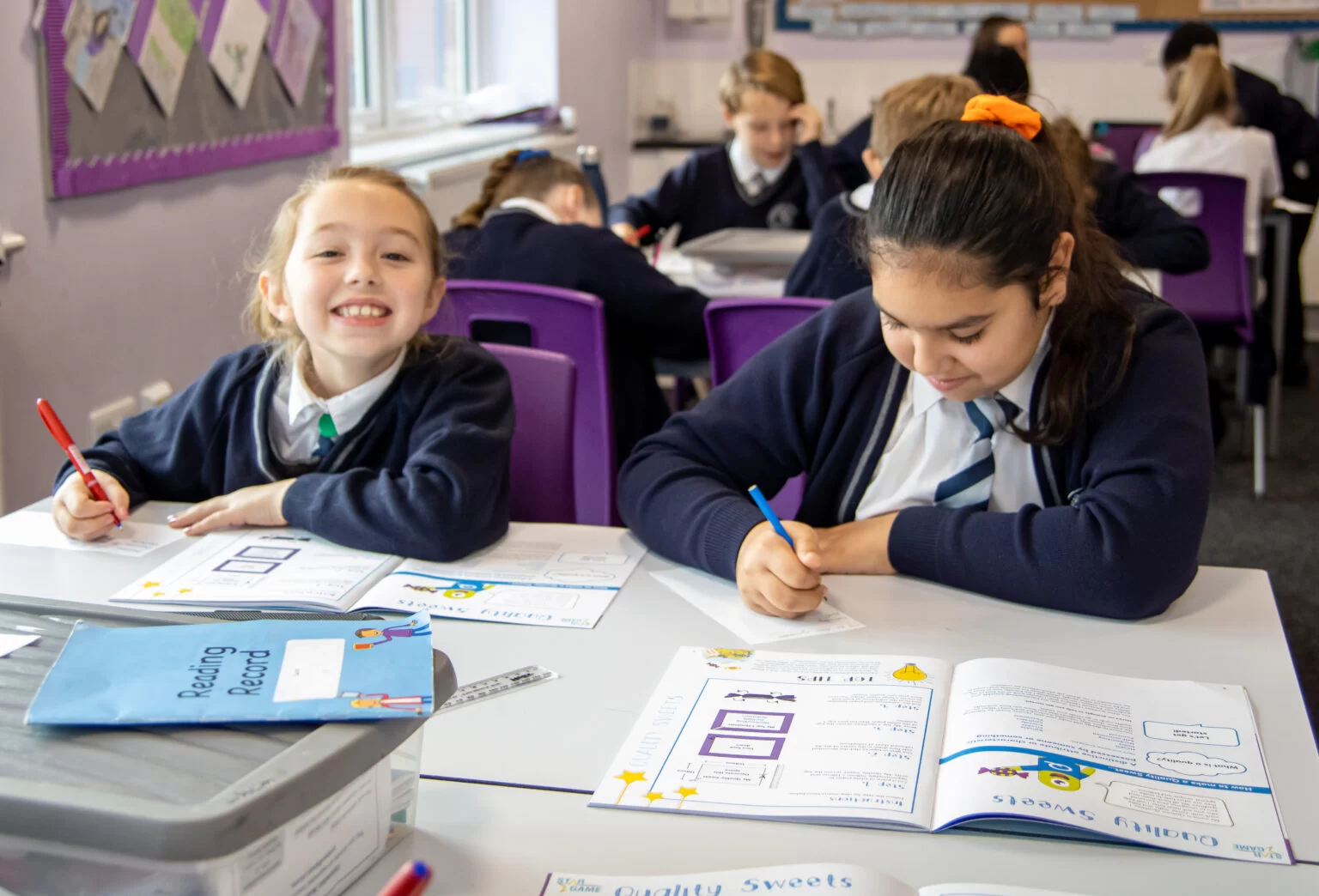 Two pupils smiling while working with a positive footprints workbook