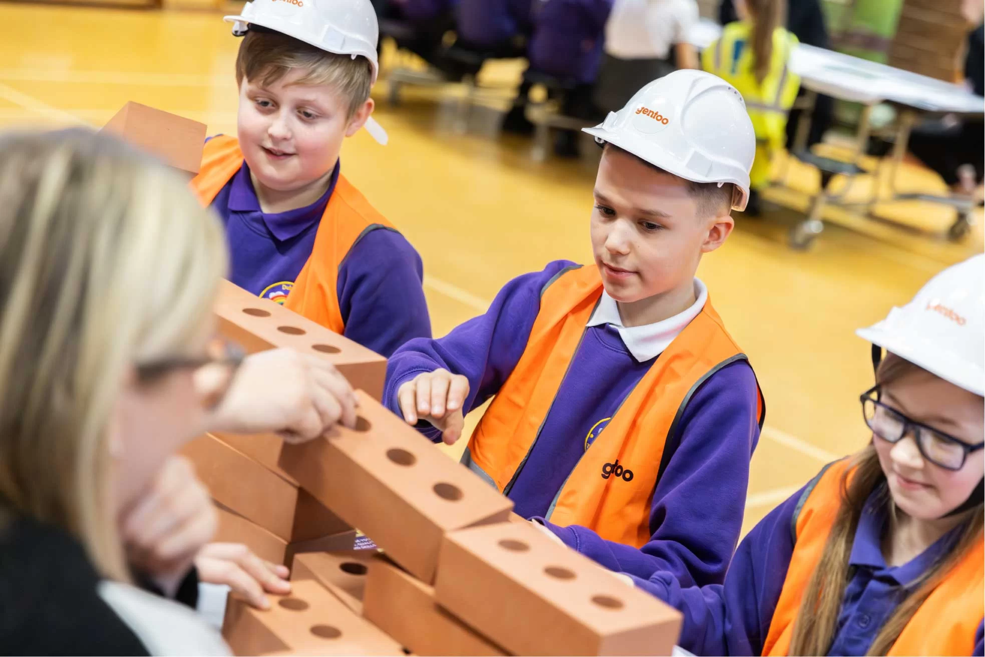 image shows a close up of a Gentoo worker and three pupils, one girl and two boys all dressed in Gentoo high-vis' jackets and hard hats