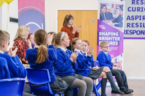 Group of young pupils in assembly hall clapping