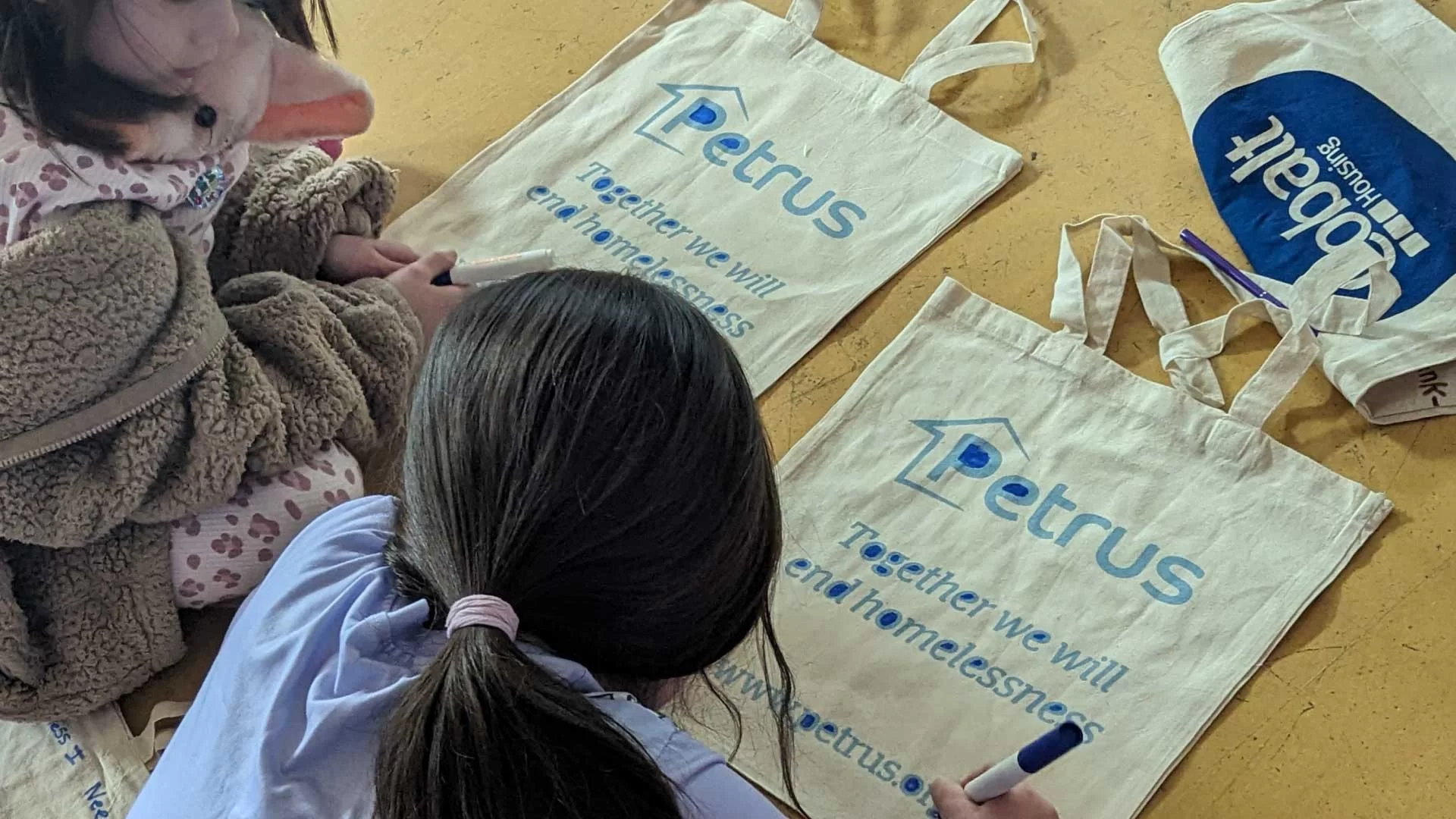 Sleep out to help out event, image of two young pupils drawing on a Petrus canvas bag to make it look prettier