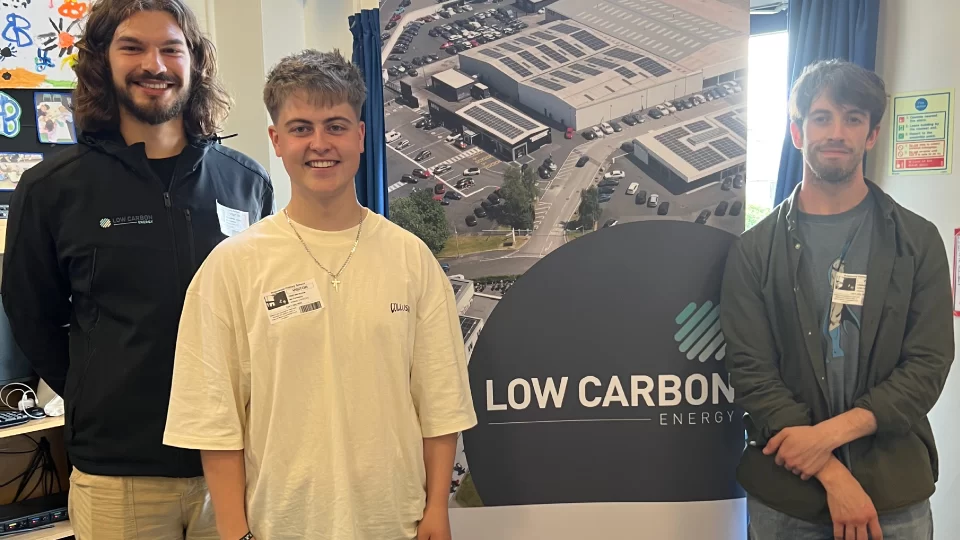 Three men smiling while standing in front of a pull up banner with the words 'low carbon energy'.