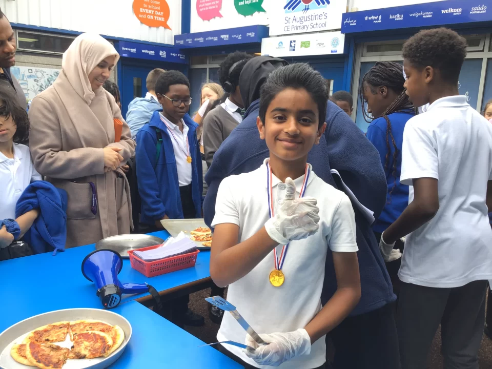 A pupil gives a thumbs up to the camera while serving Pizza