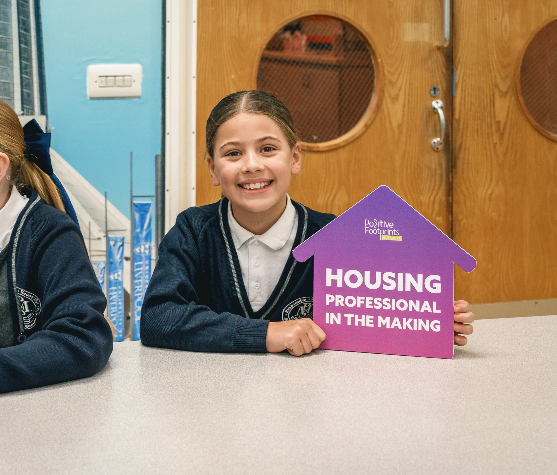 A girl smiles and holds a card that says "Housing Professional in the making"
